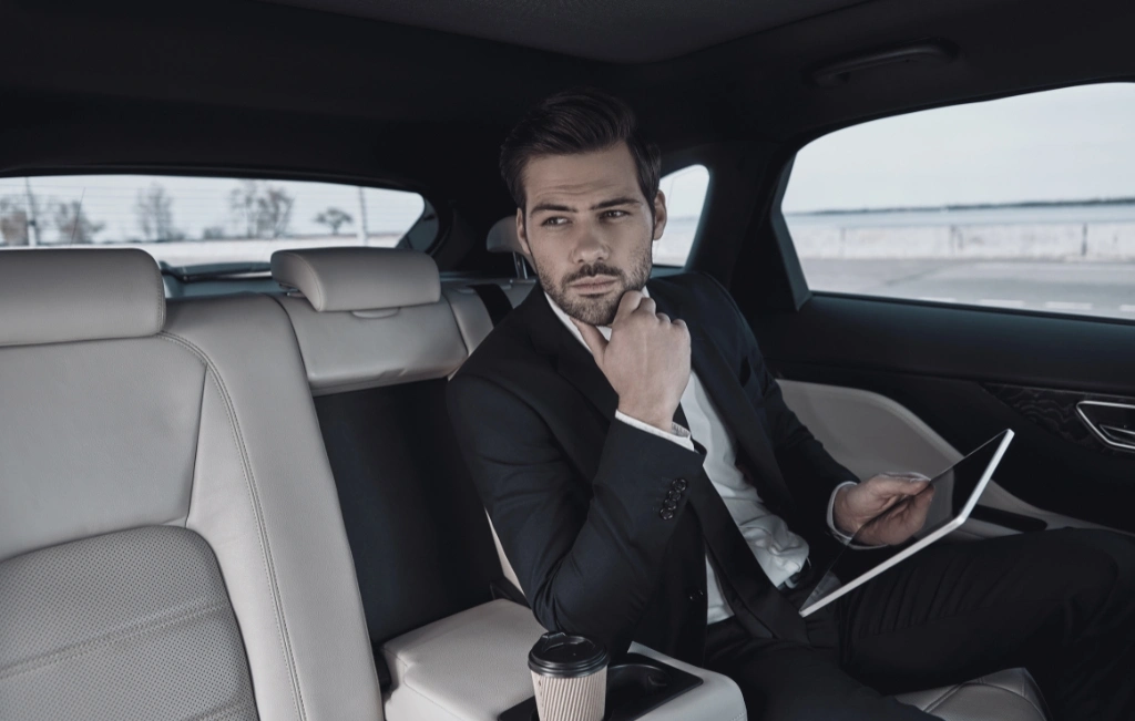 Businessman in full suit working using digital tablet while sitting in the car during his limo chauffeur service
