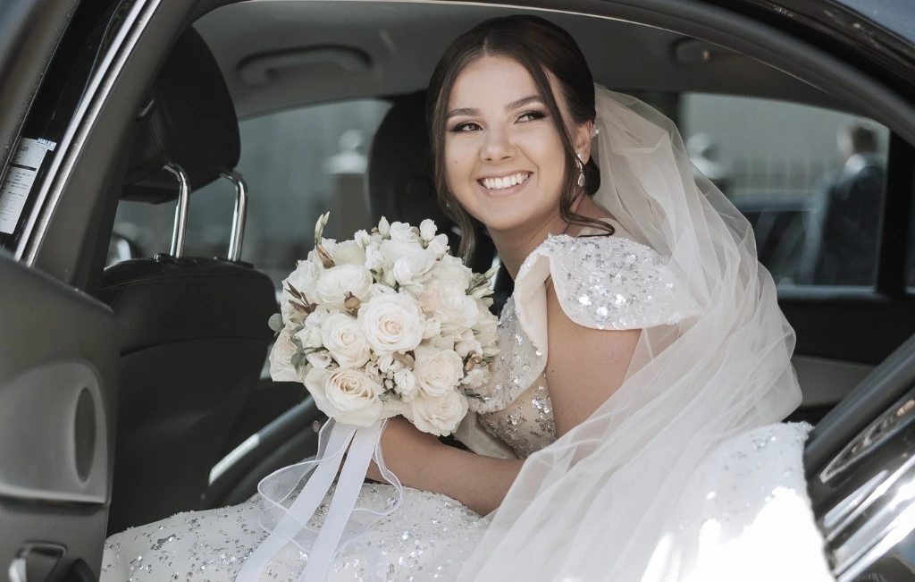 bride sitting in a black car with a bouquet of flowers